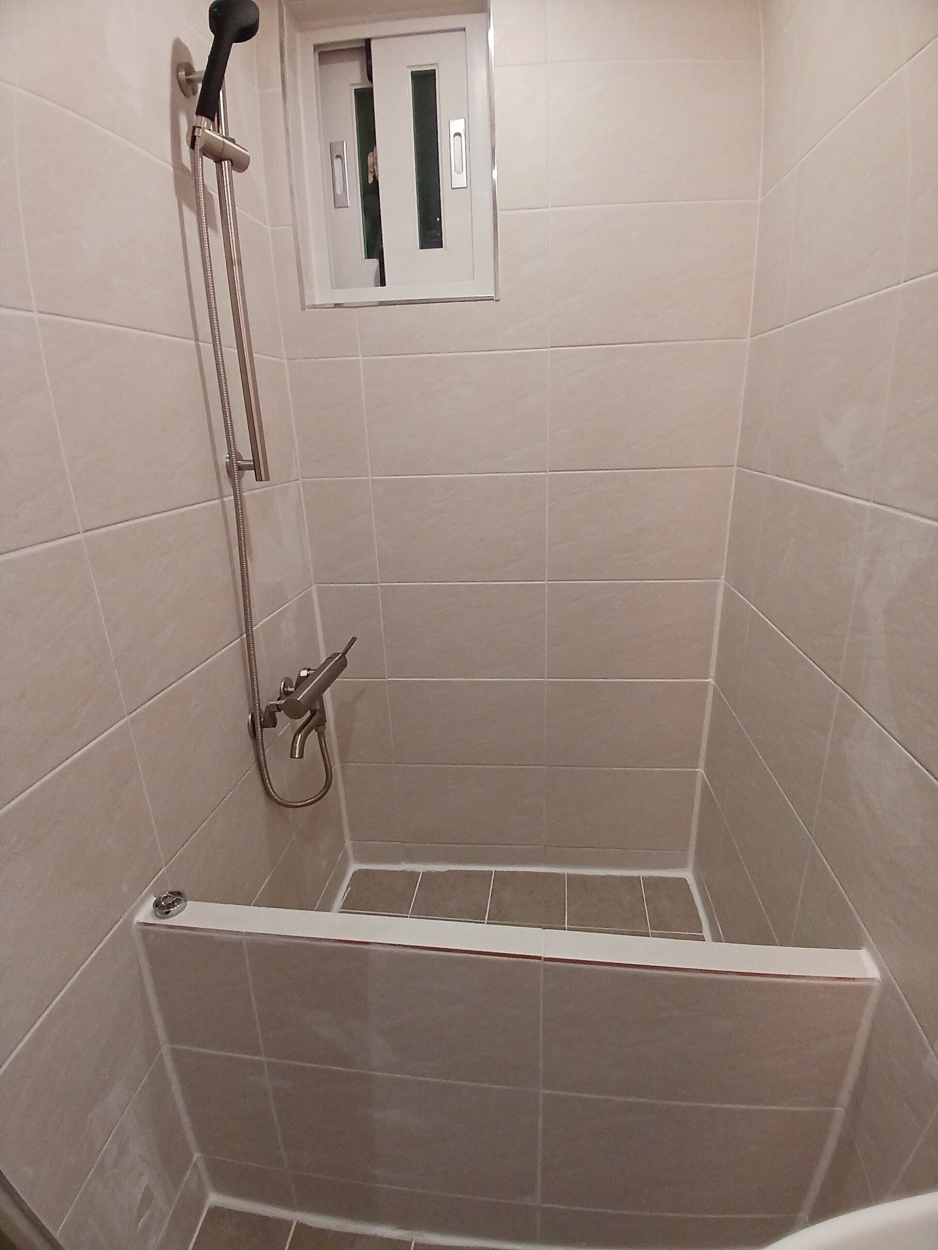 A shower with a handheld showerhead, a wall-mounted faucet, and a small window.