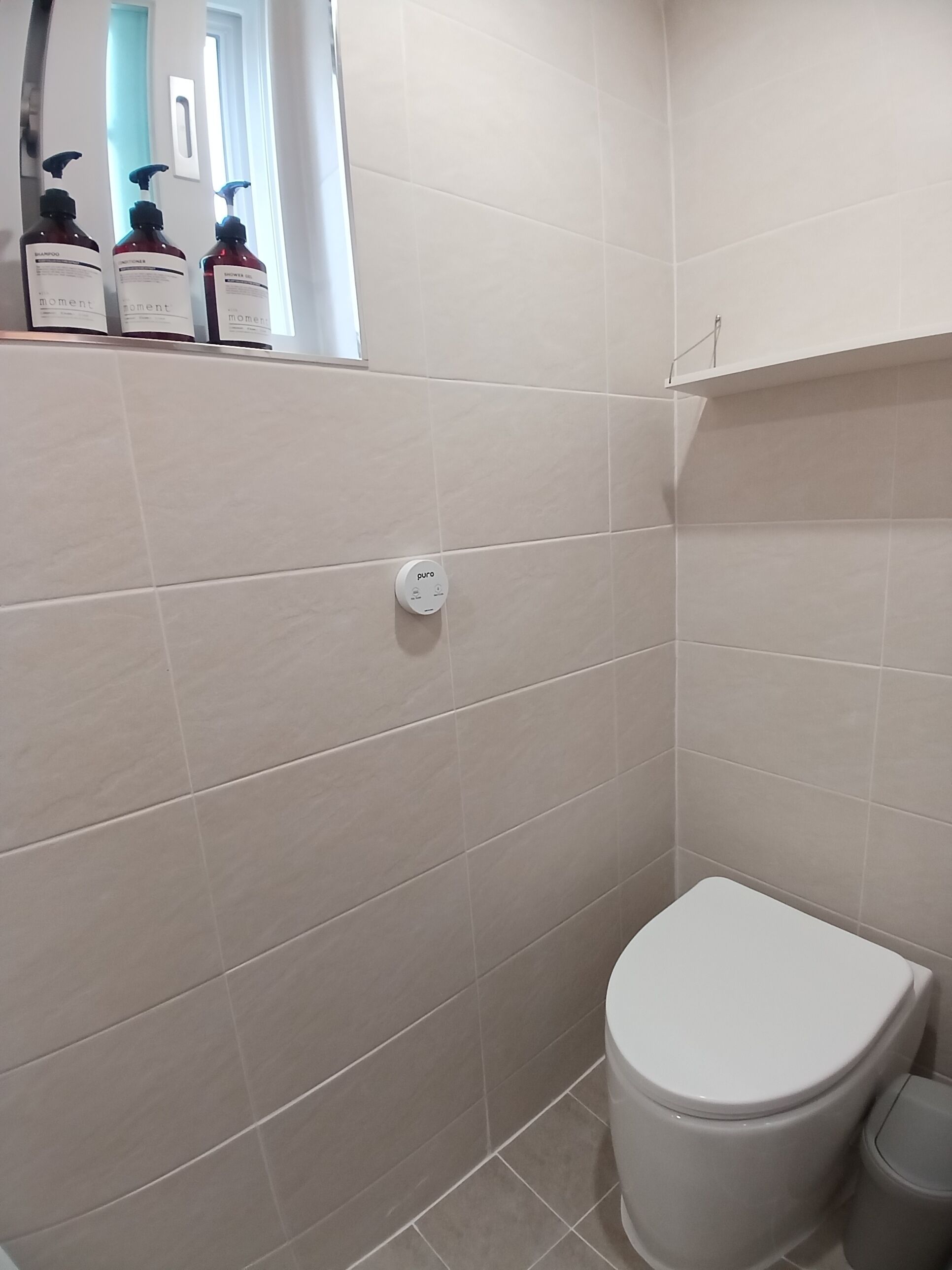 Ett badrum med en toalett, en väggmonterad kontrollpanel och en hylla med toalettartiklar.