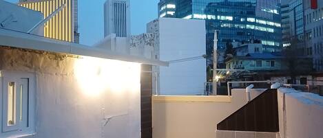 A rooftop terrace with a table and chairs, a view of modern buildings, and a clear sky.