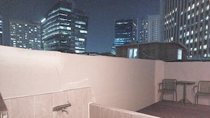 Terraza en la azotea con un espacio de descanso, un muro de baldosas y vistas a edificios iluminados por la noche.