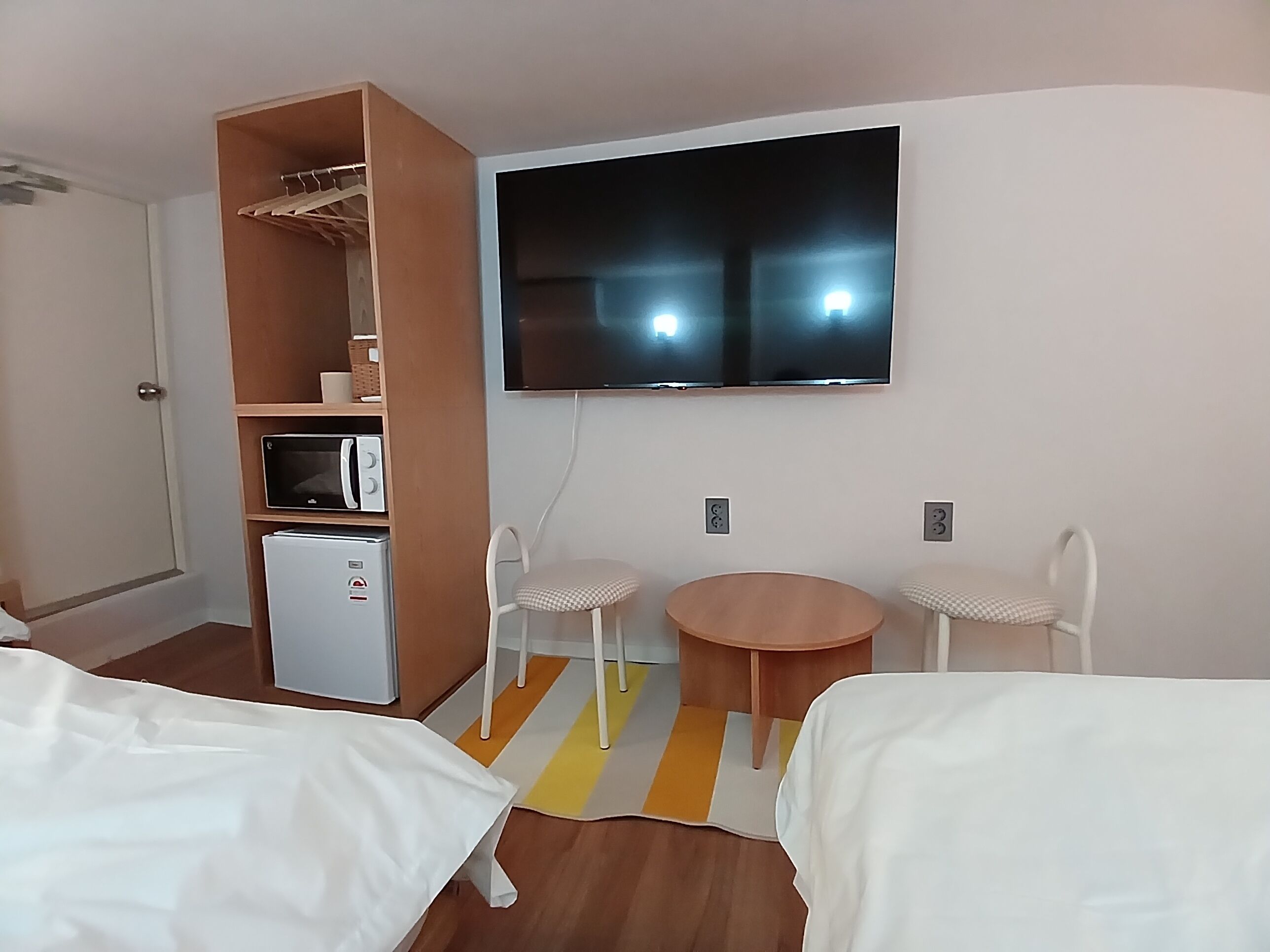 Habitació d'hotel amb dos llits, un petit frigorífic, microones, televisió i zona de seients amb cadires i taula.