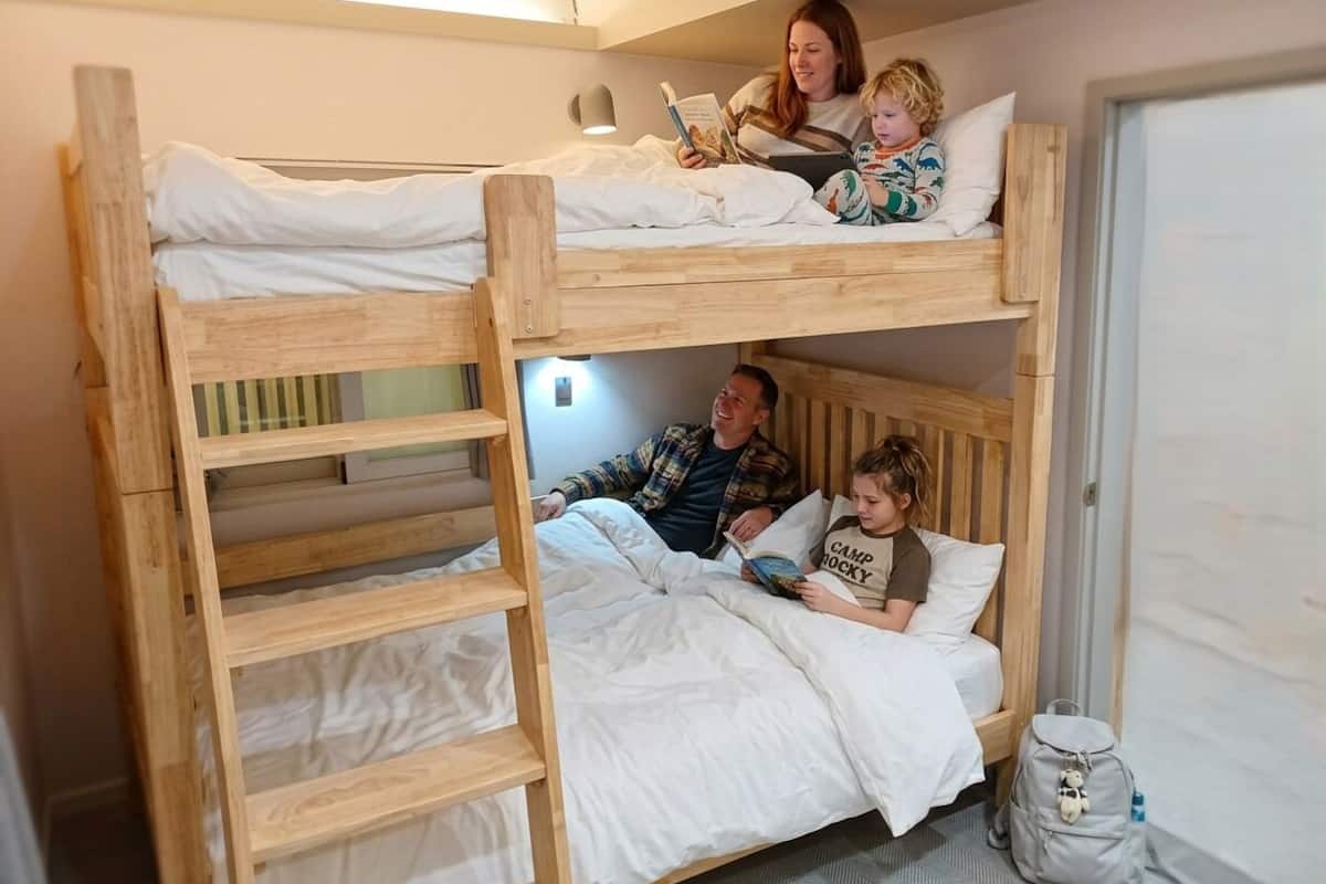 Habitació amb literes, una làmpada de nit i una motxilla a terra.