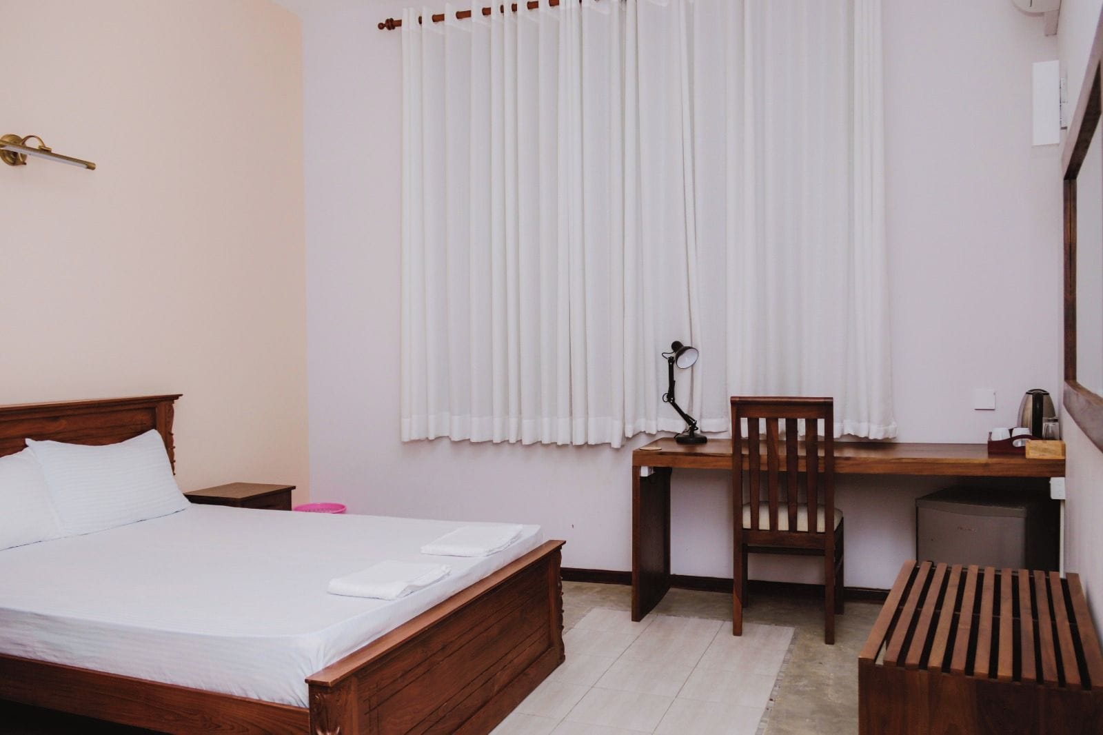 A bedroom with a wooden bed, a desk with a chair, a lamp, and a small table.