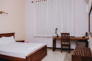 Un dormitorio con una cama de madera, un escritorio con silla, una lámpara y una mesita.