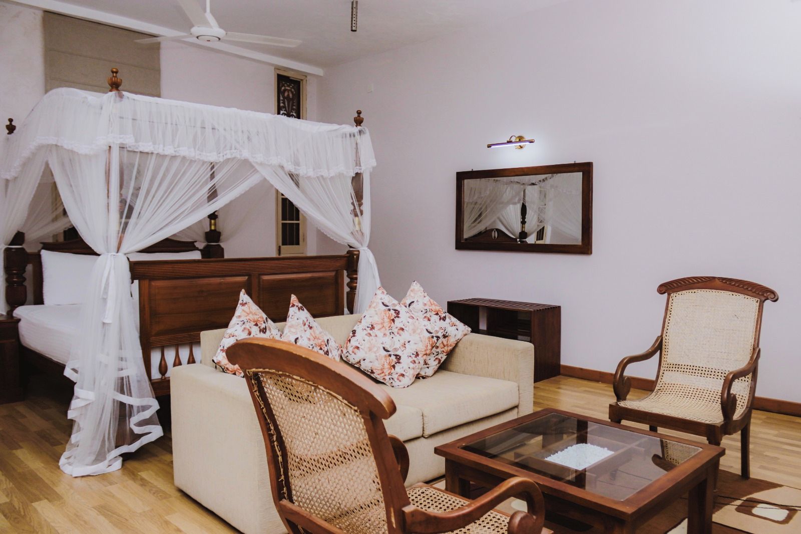 Un dormitorio con cama con dosel, un sofá, dos sillones, una mesa de centro y un espejo en la pared.