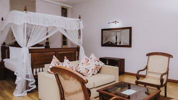 Un dormitorio con cama con dosel, un sofá, dos sillones, una mesa de centro y un espejo en la pared.