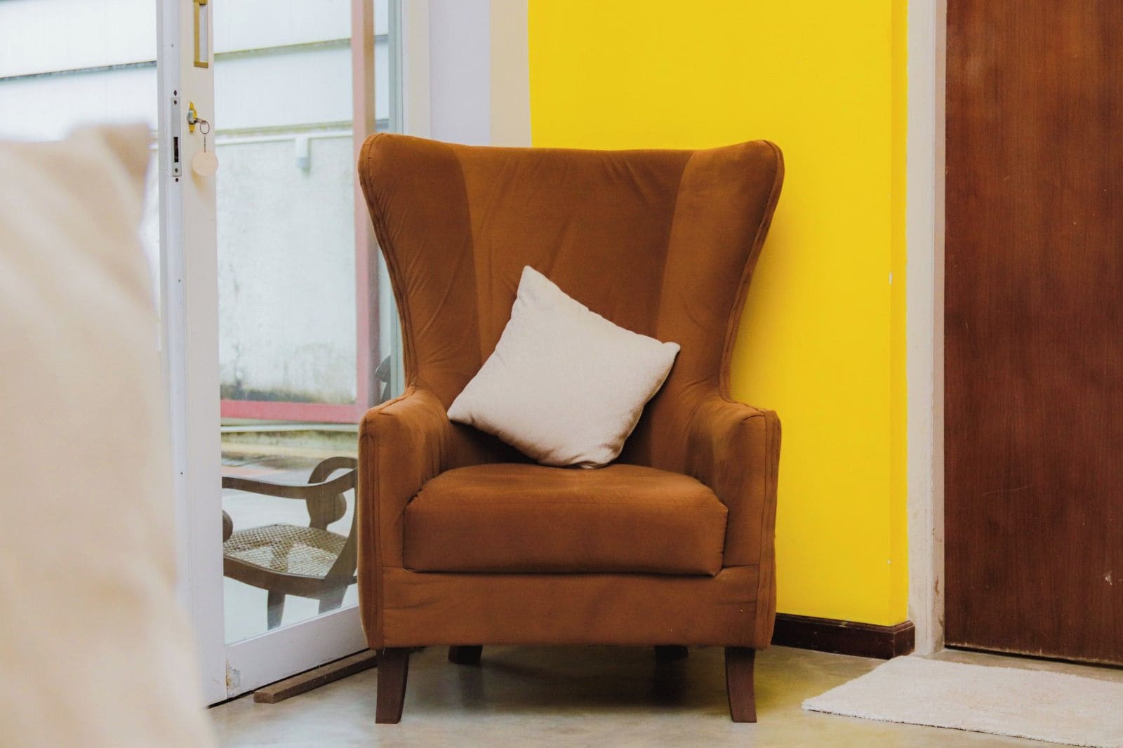 A brown armchair with a white pillow in a room with a yellow wall and a wooden door.