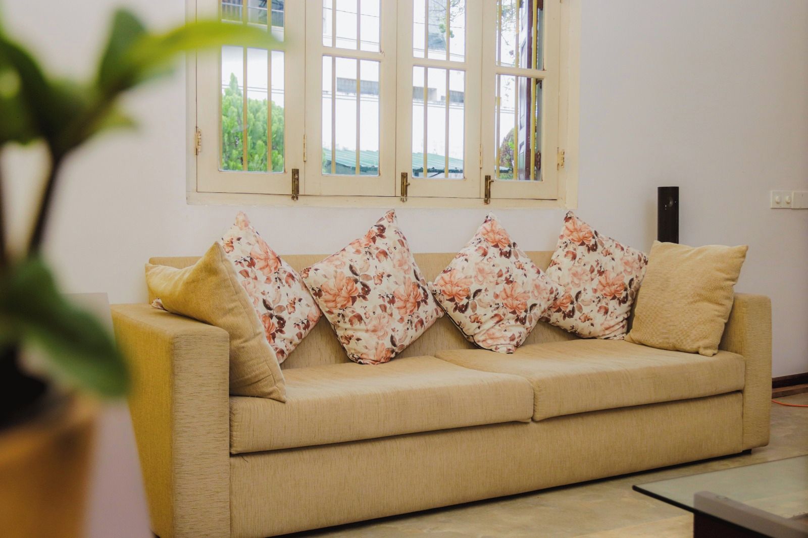 A beige sofa with floral cushions and a window with multiple panes.