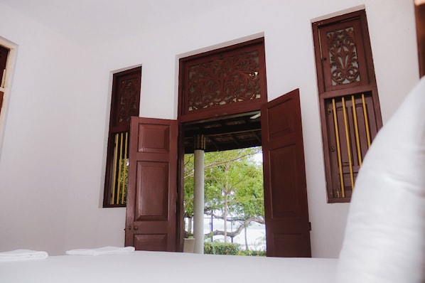 A room with a bed, a window with wooden shutters, and a view of greenery outside.