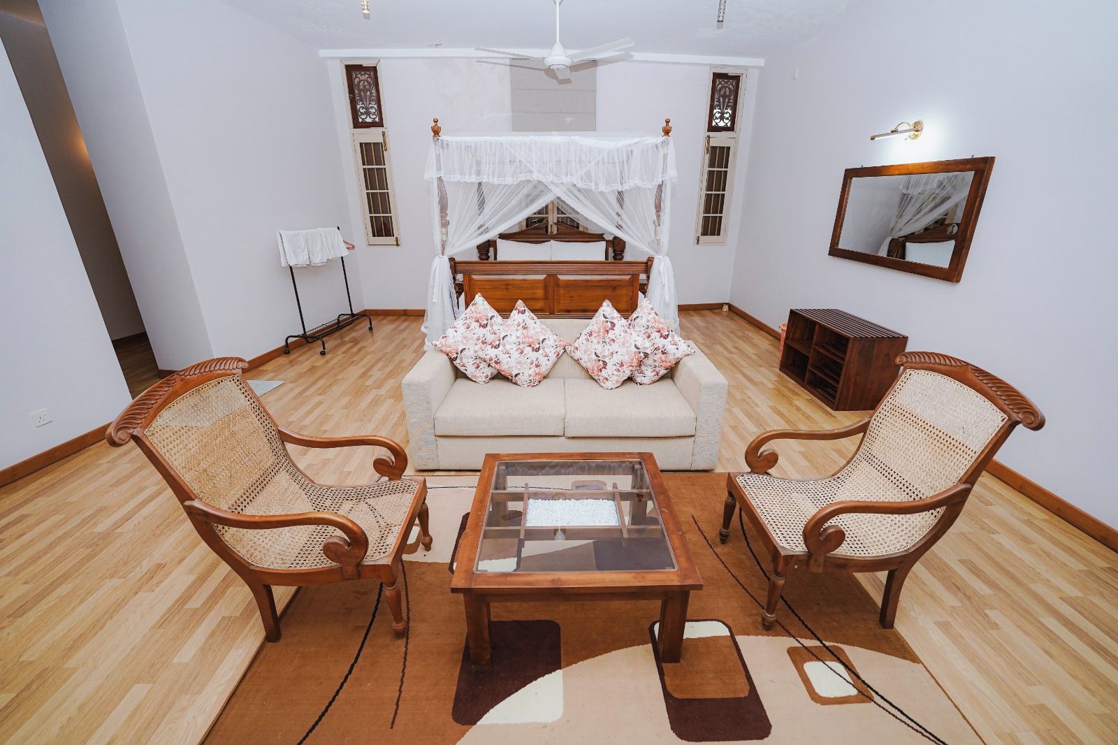 A room with a bed, two wicker chairs, a coffee table, and a ceiling fan.