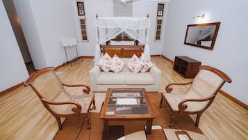A room with a bed, two wicker chairs, a coffee table, and a ceiling fan.
