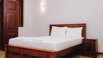 A neatly made bed with white linens and pillows, a wooden headboard, and a small bedside table with a drawer.
