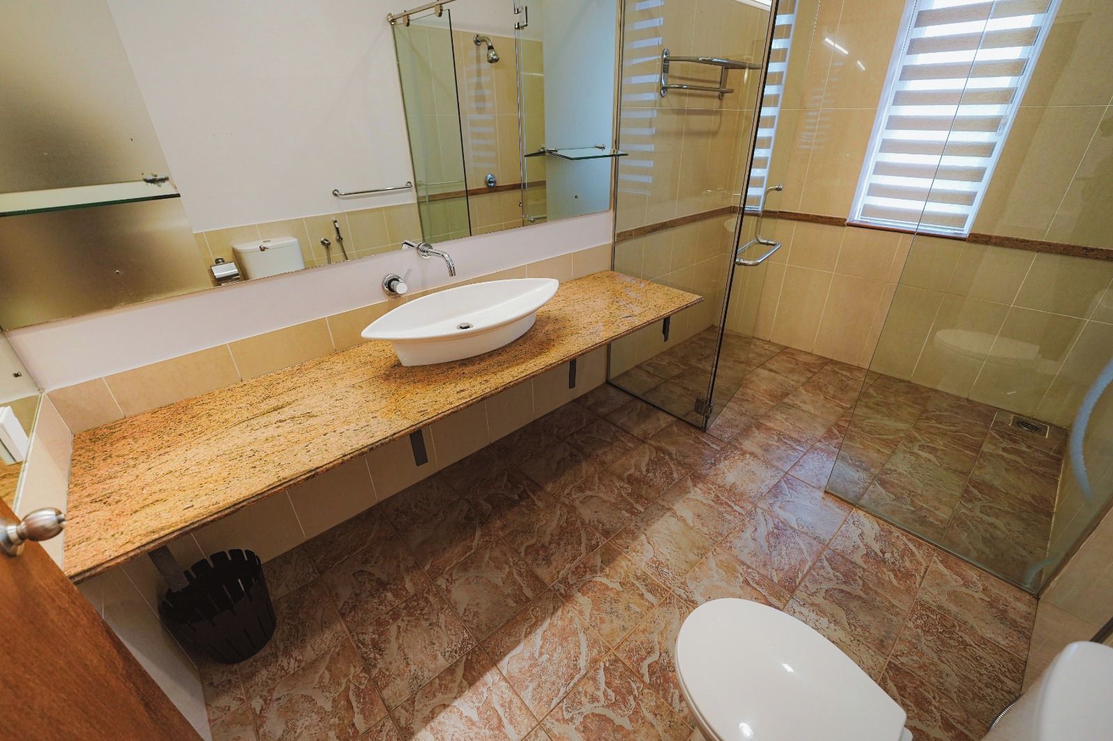 A bathroom with a granite countertop, a white sink, a glass shower enclosure, and a toilet.