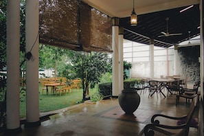 An indoor area with tables and chairs, a large potted plant, and a view of a garden.