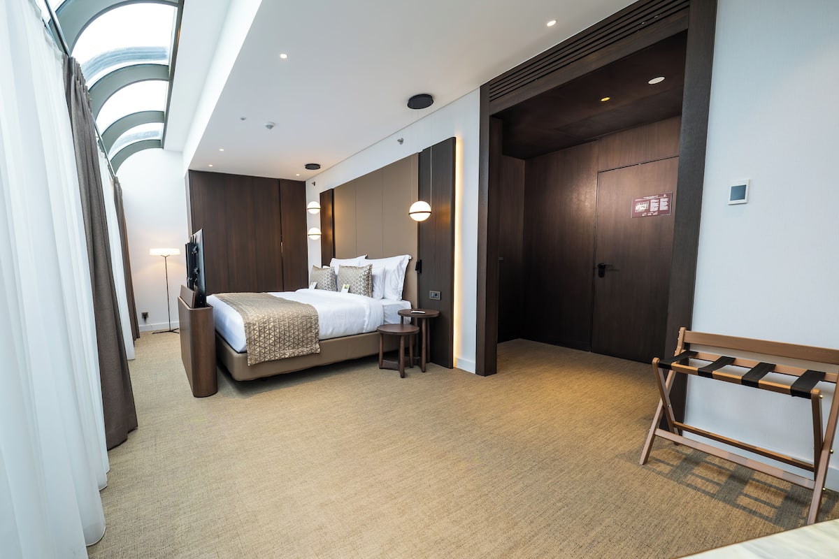 A modern hotel room with a large bed, bedside tables, a TV, and a wooden bench.