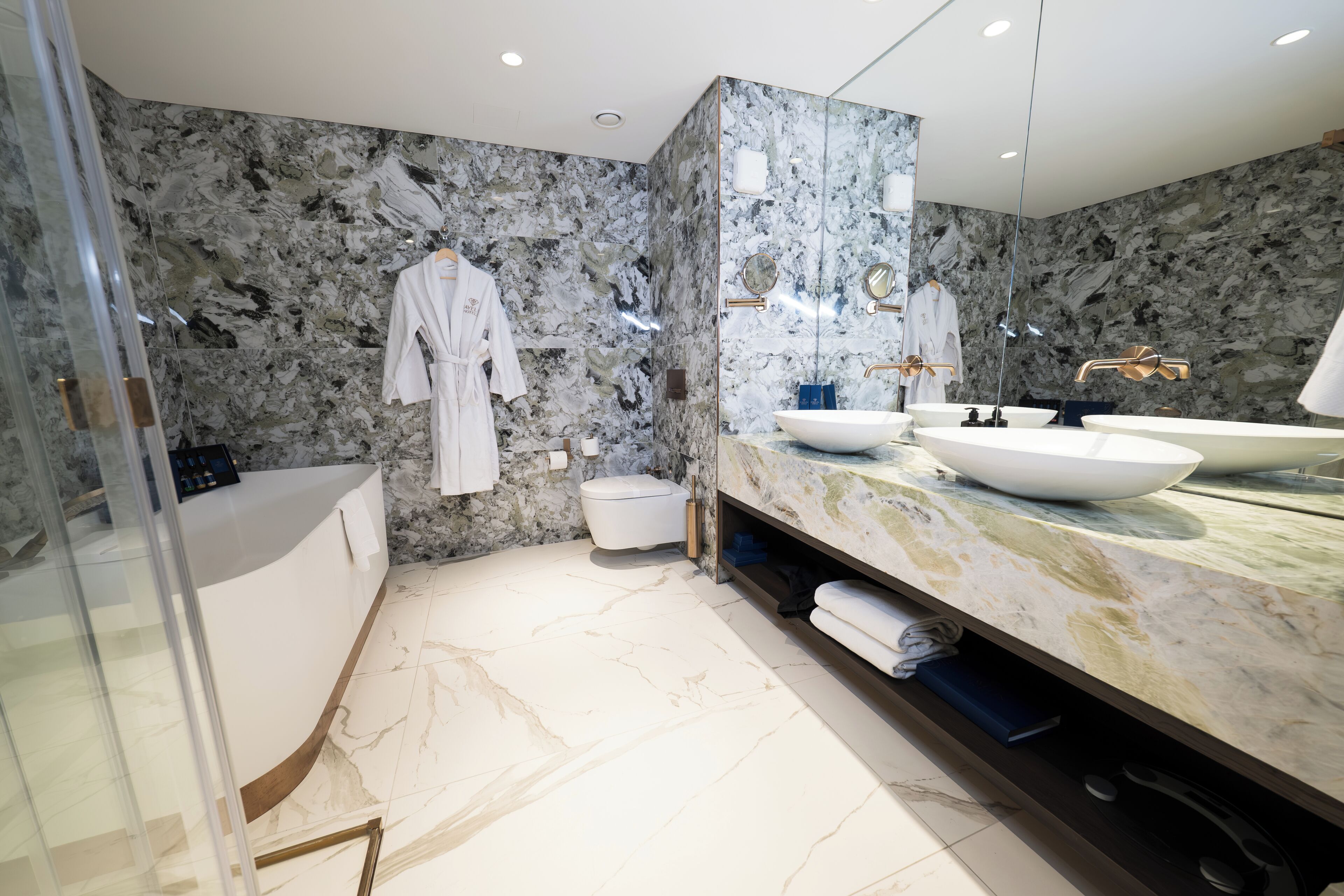 A modern bathroom with a marble backsplash, a glass shower enclosure, and a vanity with two sinks.