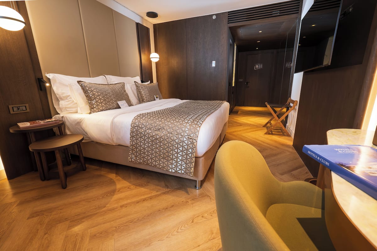 A hotel room with a bed, a desk, a chair, and a mirror.