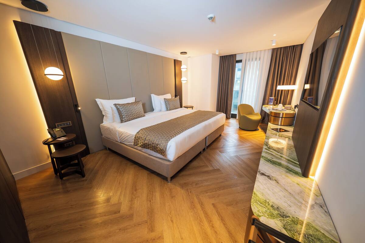 A modern hotel room with a large bed, a desk with a chair, a round table, and a large mirror.