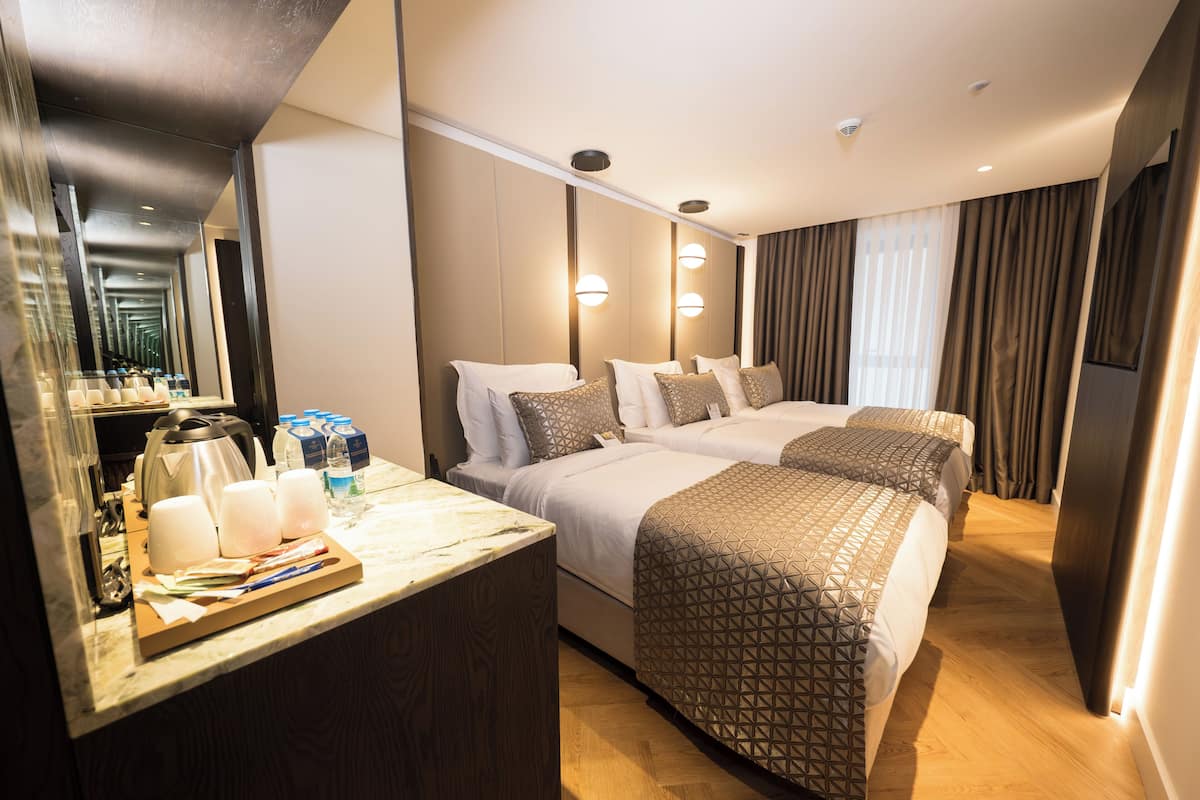A hotel room with two beds, a wooden desk with a coffee maker, and a mirror.