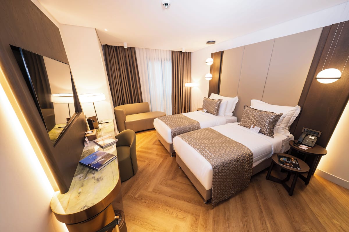 A hotel room with two beds, a desk, a chair, a desk lamp, a telephone, and a mirror.
