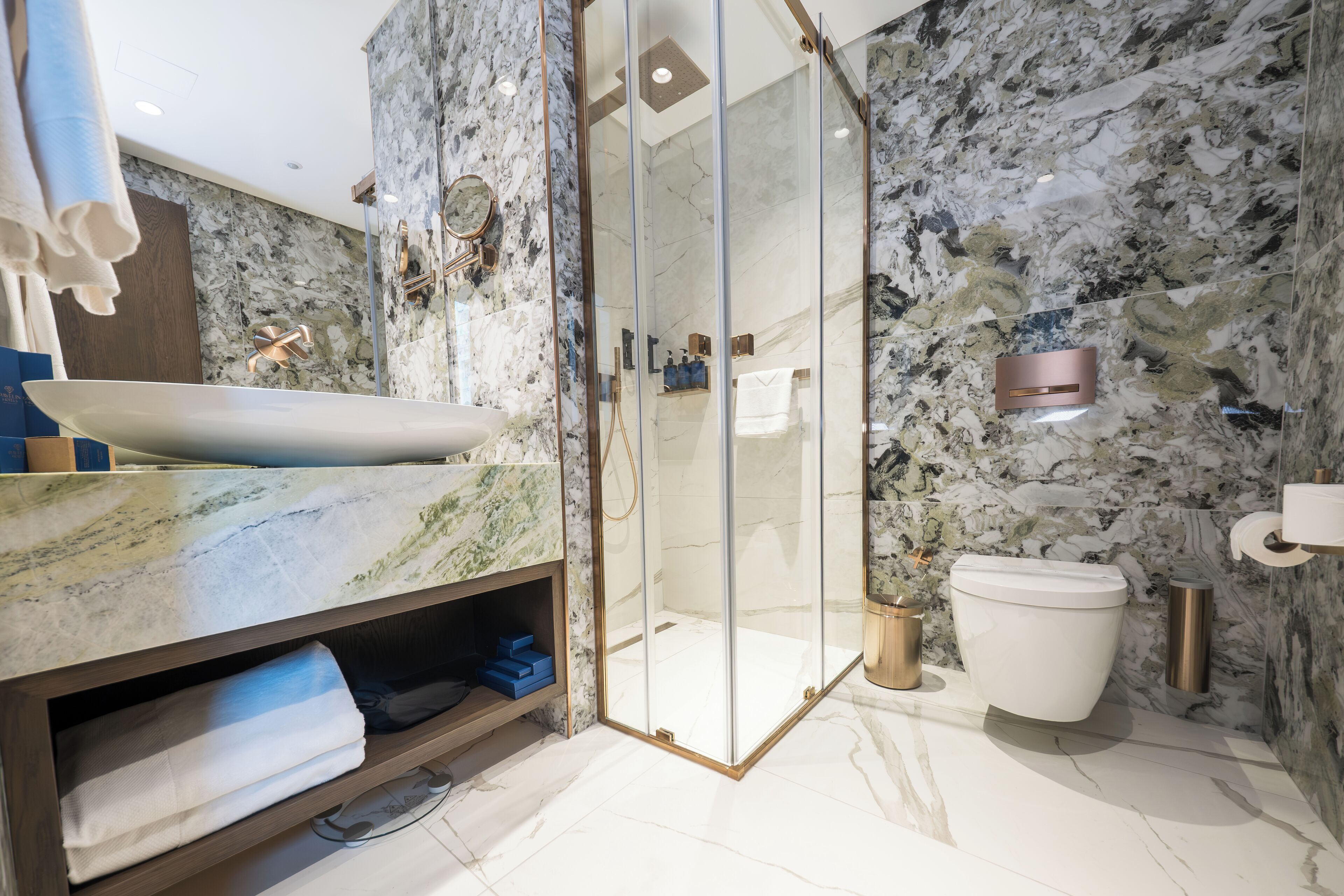 A modern bathroom with a marble sink, a glass-enclosed shower, and a toilet.