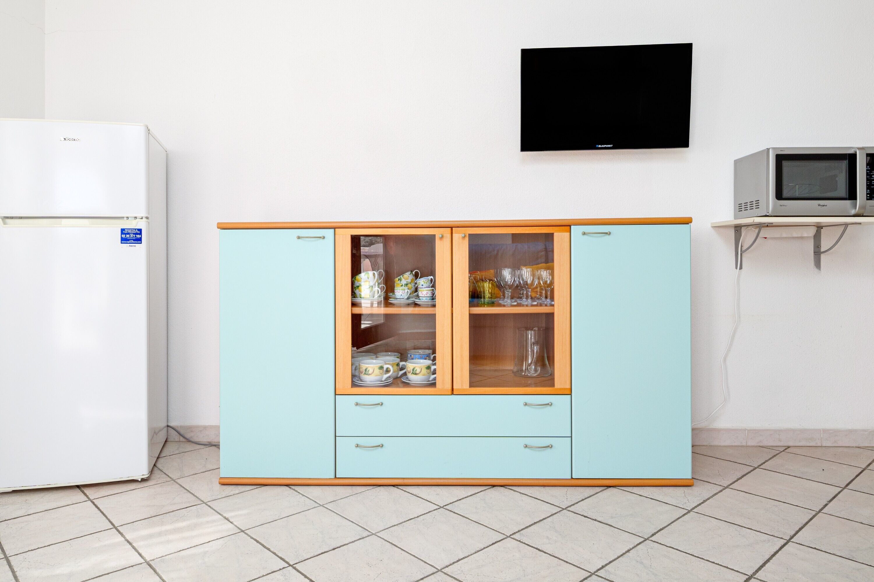 A kitchen with a white refrigerator, a light blue cabinet with glass doors, and a microwave on a shelf.