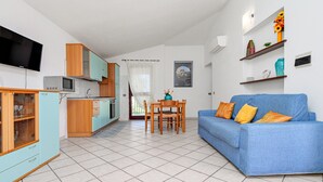 Een moderne woonkamer met een blauwe bank, een houten eettafel en een keuken met kasten en een televisie.