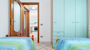 Een slaapkamer met twee bedden, een kledingkast en uitzicht op de keuken.