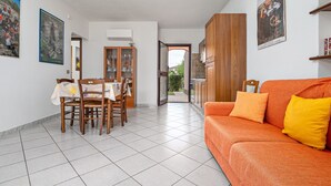 A dining area with a table and chairs, a sofa, and a kitchen visible through an open doorway. - Apartment 'Sardegnadream 6' with Private Terrace, Wi-Fi and Air Conditioning (Suaredda-traversa)