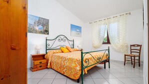 Une chambre à coucher avec un lit, une table de chevet, une chaise et une fenêtre avec des rideaux.