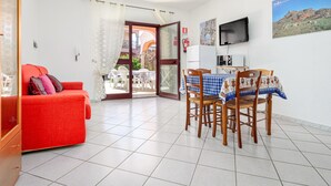 Une pièce avec un canapé rouge, une table à manger avec des chaises, un téléviseur et une grande fenêtre donnant sur un immeuble.