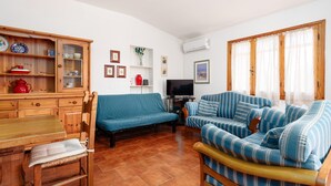 Uma sala de estar com sofá, um armário de madeira, uma televisão e uma mesa de jantar.