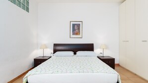 Um quarto com cama, duas mesas de cabeceira, um criado-mudo, cabeceira e um guarda-roupa.