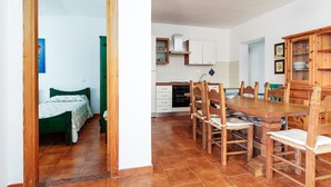 Um quarto com cama, uma mesa de jantar de madeira com cadeiras, uma cozinha com armários e fogão, e um banheiro pequeno.