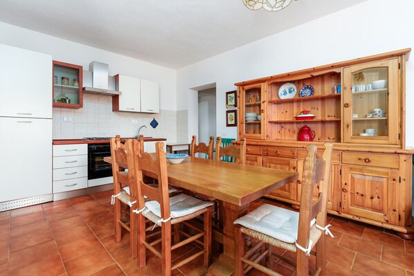 Una cocina con una mesa de madera, sillas, armarios y un hervidor rojo.
