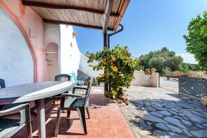 A patio with a table and chairs, a potted plant, and a stone pathway leading to a building. - Orosei Domo Holiday Home with Mountain View, Private Terrace & Air Conditioning (Orosei)