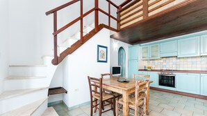 Una cucina con mobili color petrolio, un tavolo da pranzo in legno e una scala con ringhiere in legno.