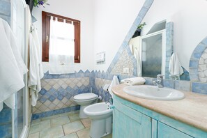 Een badkamer met een douche, toilet, bidet, wastafel en een spiegel.