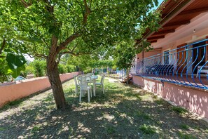 A patio with a table and chairs, a tree, and a building with a blue railing. - Holiday Home 'Le Campanelle a Fuile Mare' with Private Terrace, Wi-Fi and Air Conditioning (Sas Linnas Siccas)