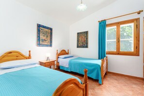 Una stanza con due letti in legno, una finestra con tende e due quadri appesi al muro.