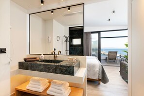 Ein modernes Hotelzimmer mit einem großen Bett, einem Badezimmer mit Marmorwaschbecken und einem Balkon mit Meerblick.