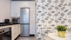 Una cocina moderna con armarios blancos, un refrigerador de acero inoxidable, un microondas y un horno. Hay una mesa de comedor blanca con una olla dorada encima.