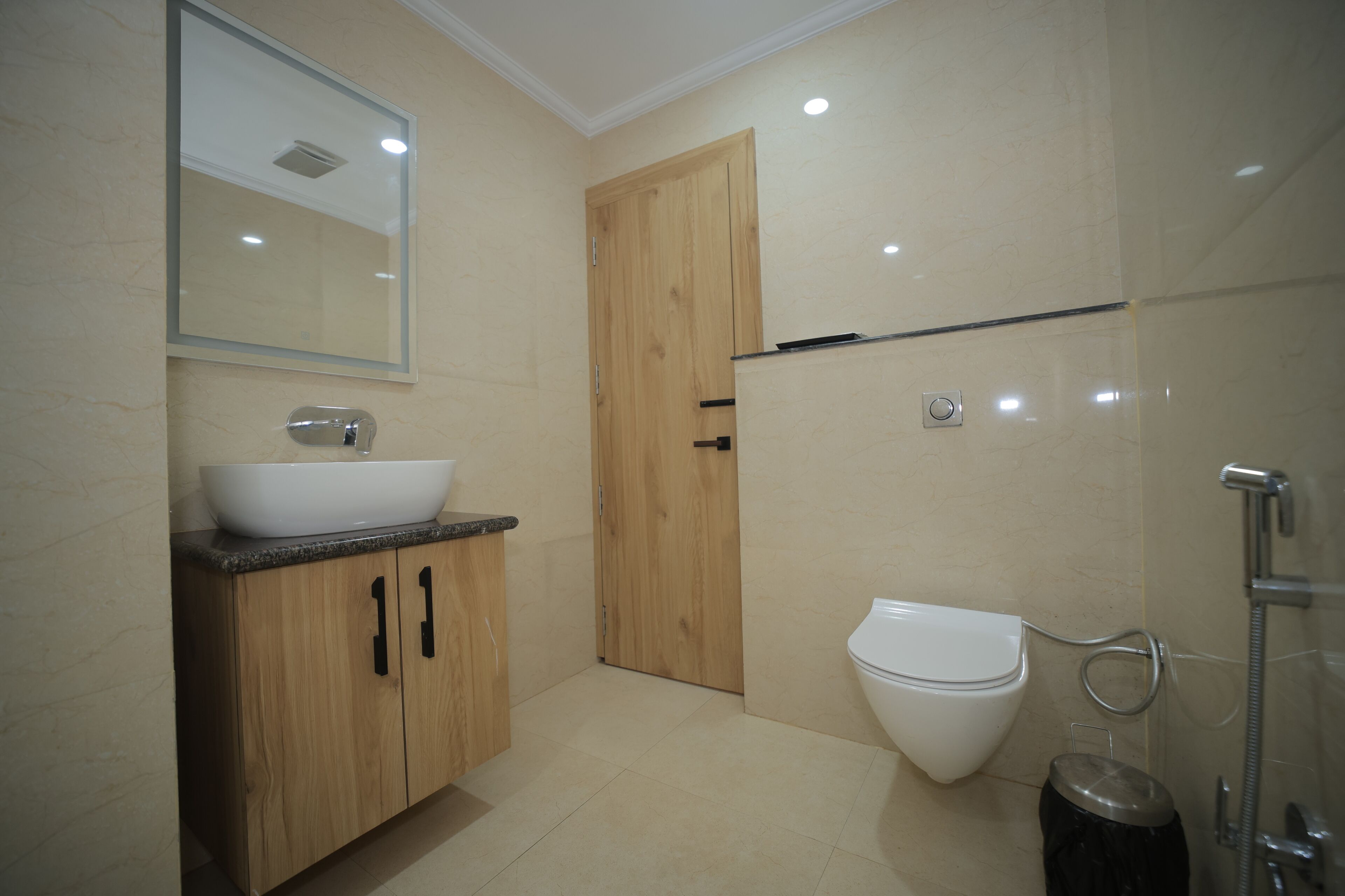A modern bathroom with a wooden vanity, a white sink, a toilet, and a shower area.