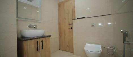 A modern bathroom with a wooden vanity, a white sink, a toilet, and a shower area.