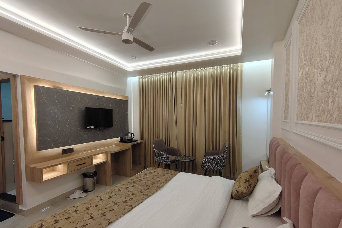 Una habitación de hotel moderna con una cama, un escritorio con televisor de pantalla plana, un ventilador de techo y un gran ventanal con cortinas.