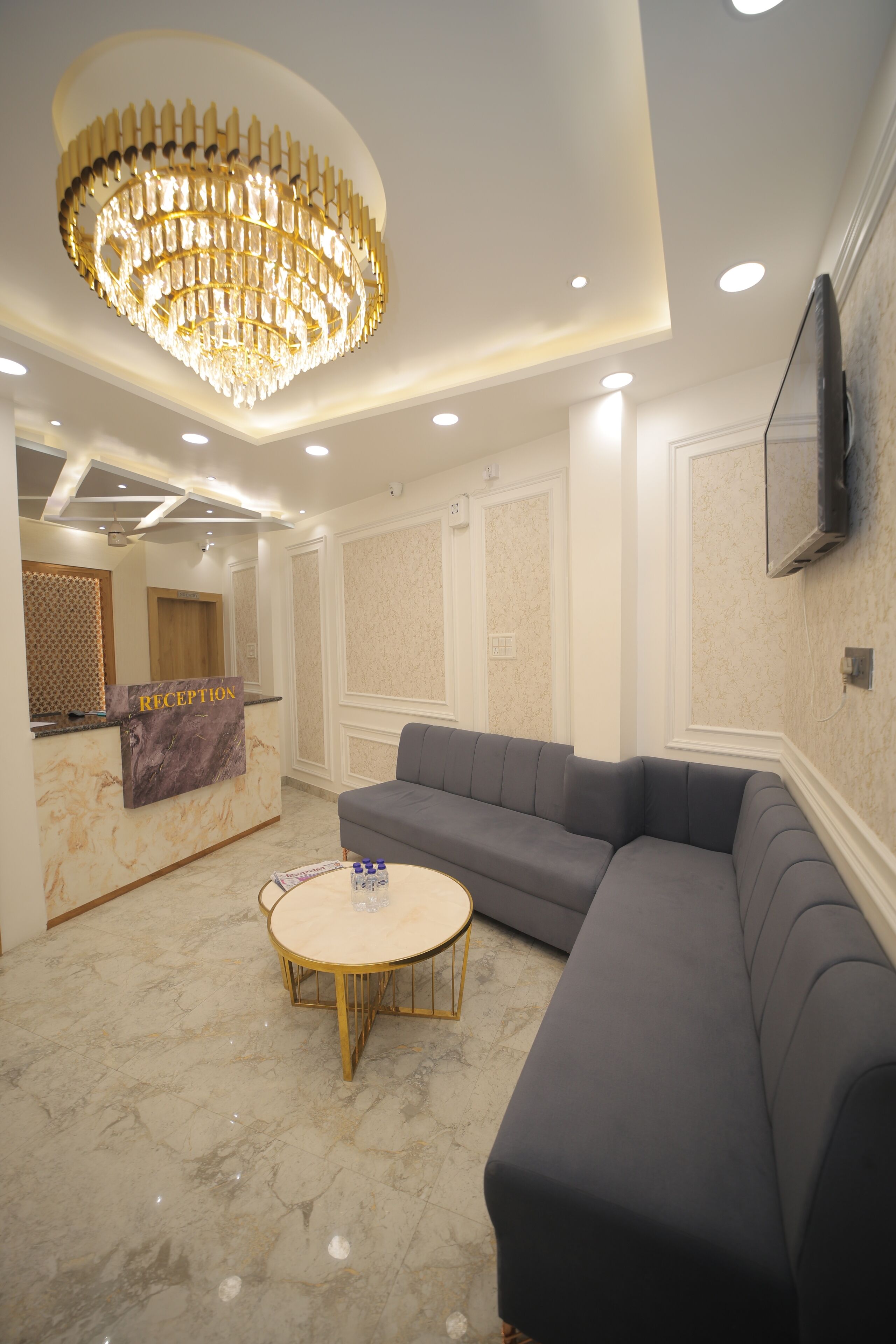A reception area with a marble counter, a large chandelier, a grey sofa, and a round table.