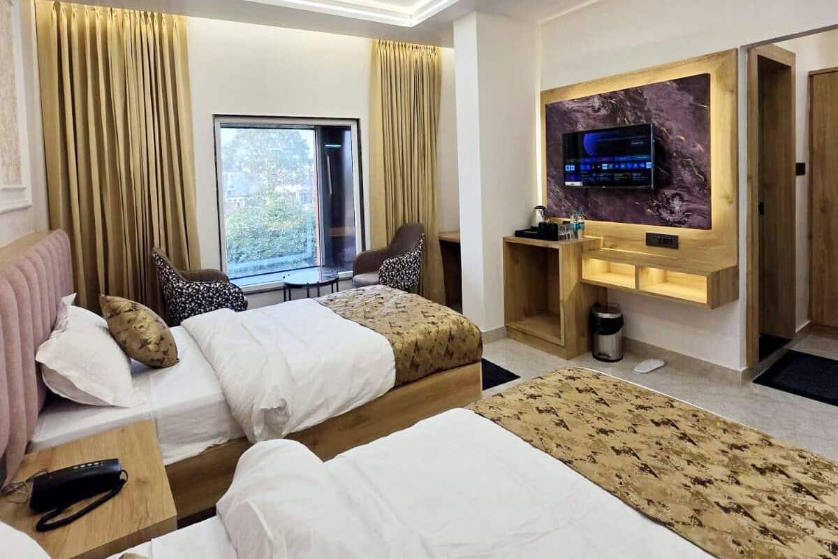 Habitación de hotel con dos camas, ventilador de techo, televisión y ventana con cortinas.