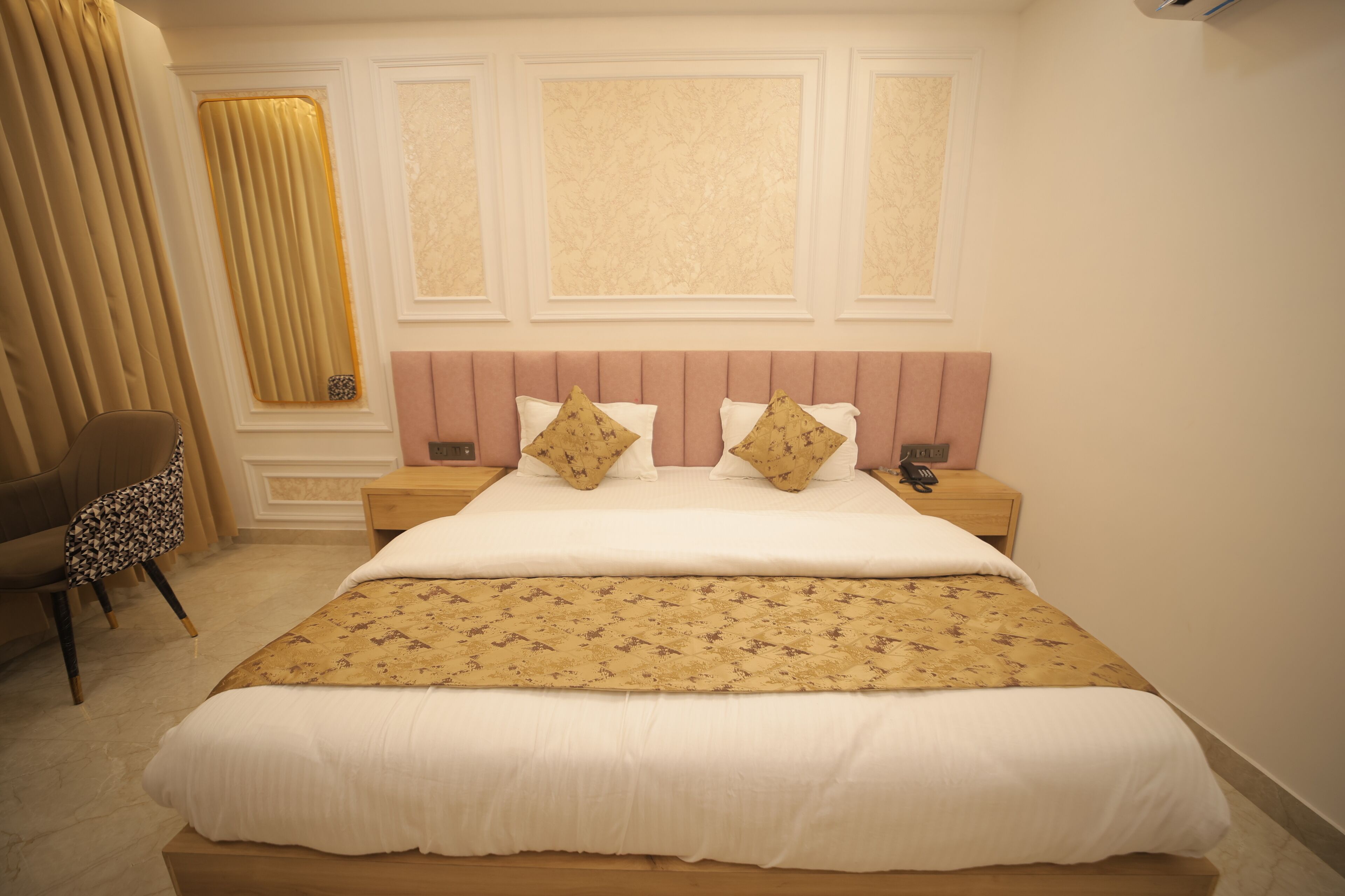 A neatly made bed with a patterned bedspread, a headboard with decorative panels, and a chair with a floral cushion.