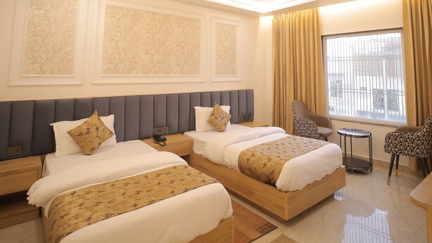 A hotel room with two beds, a ceiling fan, a window with curtains, and a small table. - BABA PALACE (Ayodhya)
