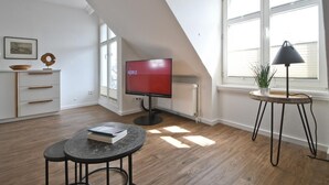 A modern living room with a TV, a round table, and a plant by a window. - Vacation apartment Wangerooge (Norderney)